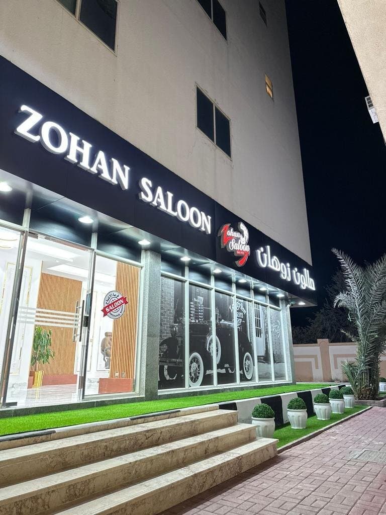 Zohan Saloon storefront signage lit up at night