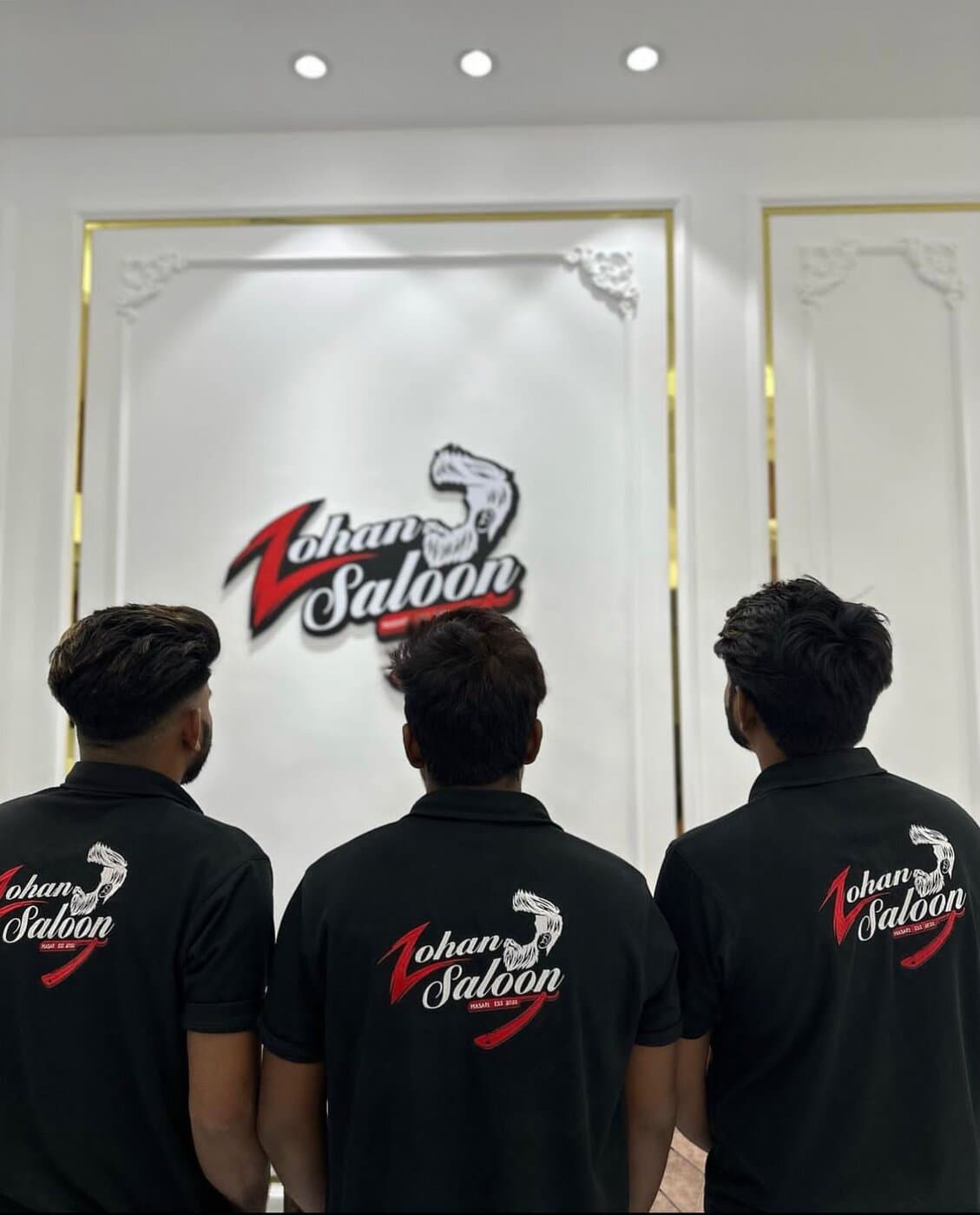 The Zohan Saloon barber team in front of the shop's logo wall
